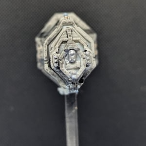 May include: A silver-colored, detailed, miniature spaceship model with a hexagonal base and a clear plastic stand.