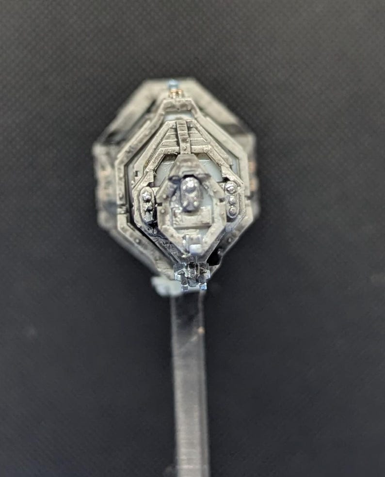 May include: A silver-colored, detailed, miniature spaceship model with a hexagonal base and a clear plastic stand.