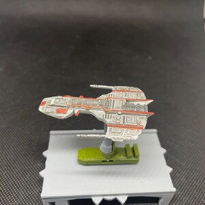 May include: A white and red spaceship model with a green base. The spaceship has a detailed design with a lot of lines and shapes.