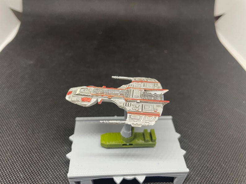 May include: A white and red spaceship model with a green base. The spaceship has a detailed design with a lot of lines and shapes.