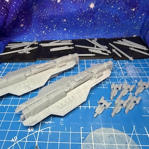 May include: A collection of unassembled gray plastic model spaceship parts. The image shows two large ship bodies, several smaller spacecraft, and various other components on a blue grid surface, with a starry background.