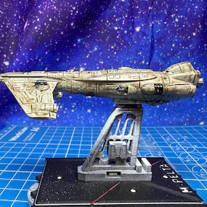 May include: A detailed model of a spaceship, painted in shades of gray and beige, mounted on a gray stand. The model has intricate detailing and is set against a starry background. The base has the text "H-PELTA".