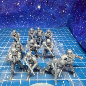 May include: A collection of gray miniature figures of soldiers in helmets and armor, holding rifles and other weapons. The figures are arranged on a blue grid surface with a starry background.