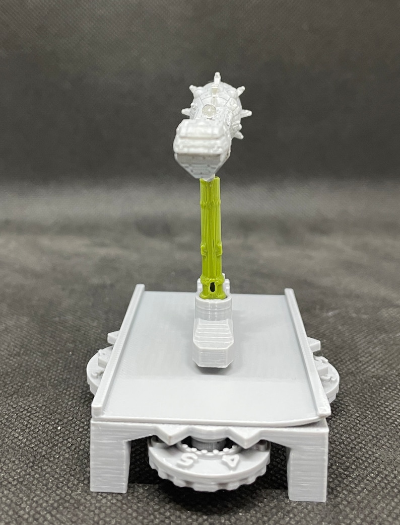 May include: A 3D printed model of a grey and green mechanical device with a spiked top. The device is mounted on a grey base with a gear system.