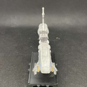May include: A silver and blue model of a spaceship with a long, thin body and a pointed nose. The model is on a black base with a textured surface.