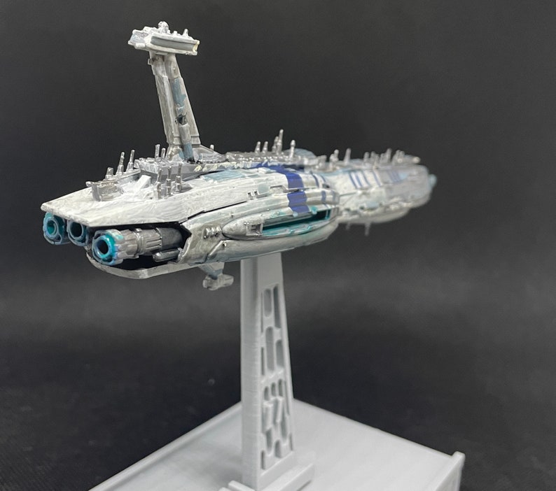 Puede incluir: Un modelo detallado de una nave espacial blanca y azul con un soporte gris. La nave espacial tiene un cuerpo largo y estrecho con una nariz puntiaguda y un ala rectangular grande a cada lado. La nave espacial est&aacute; decorada con rayas azules y blancas.