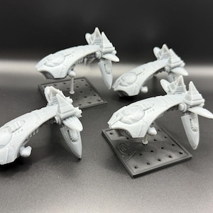 以下が含まれることがあります： 小さな黒い台座にそれぞれ取り付けられた、4つの明るい灰色の宇宙船モデル。宇宙船は、翼のような構造と詳細な表面特徴を備えた、洗練された未来的なデザインです。モデルは暗い表面に配置されています。