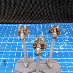 May include: Three miniature spaceships painted in a camouflage pattern with red missile launchers. The spaceships are mounted on grey bases with white plastic stands.