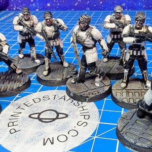 Puede incluir: Colección de figuras en miniatura de soldados con armadura blanca y negra, cada uno sosteniendo un arma. Las figuras están sobre bases circulares grises, con un logotipo impreso en el centro. El fondo es una cuadrícula azul.