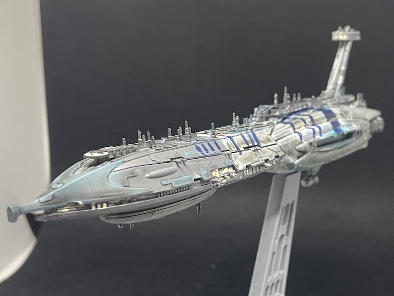 Puede incluir: Un modelo detallado de una nave espacial gris y azul con un cuerpo largo y estrecho y una nariz puntiaguda. La nave espacial tiene una serie de peque&ntilde;as estructuras cil&iacute;ndricas a lo largo de sus lados y una gran estructura rectangular en la parte trasera.