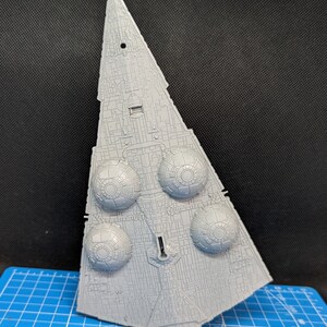 May include: A gray plastic model of a Star Destroyer spaceship. The model has a detailed design with multiple engine pods and a pointed nose.