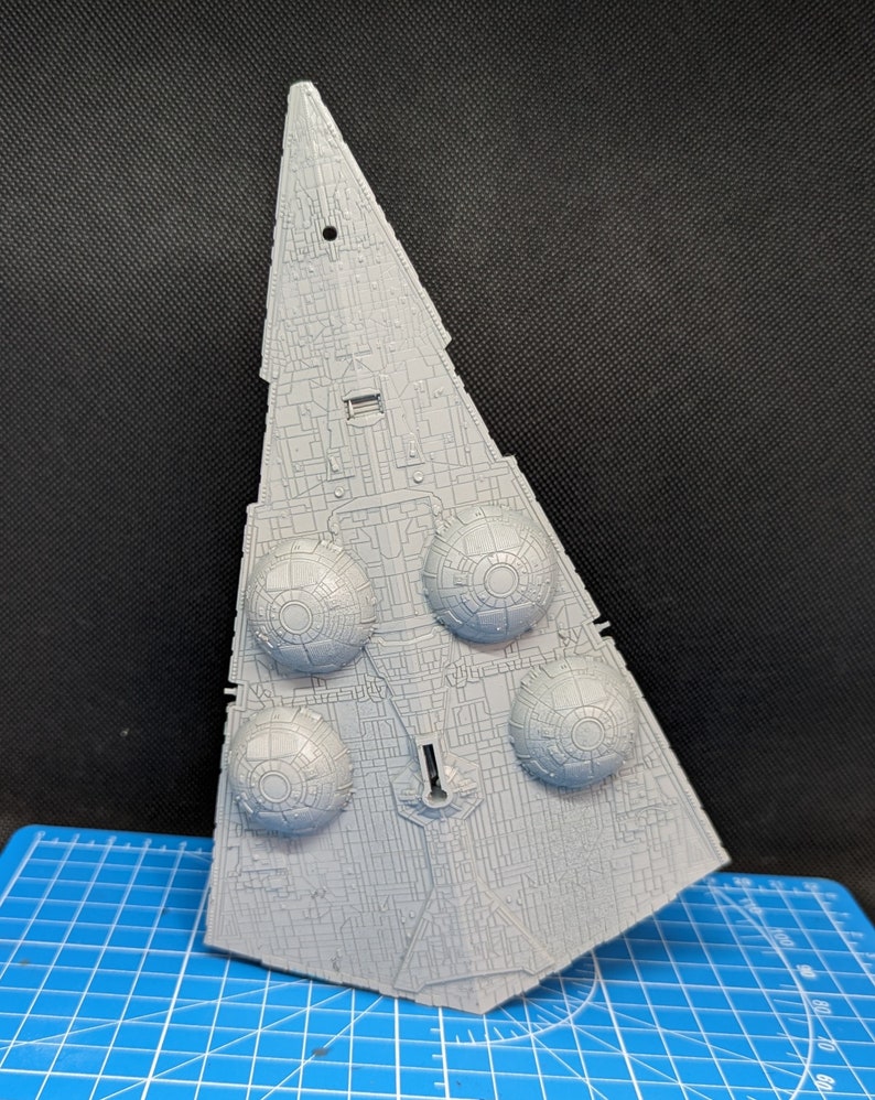 May include: A gray plastic model of a Star Destroyer spaceship. The model has a detailed design with multiple engine pods and a pointed nose.