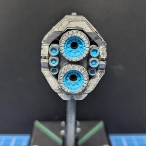 May include: A close-up of a model spaceship with a gray and silver paint finish. The spaceship has multiple blue exhaust ports on the back.