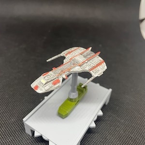 May include: A white and red spaceship model with a gray base. The spaceship has a detailed design with a variety of textures and shapes.