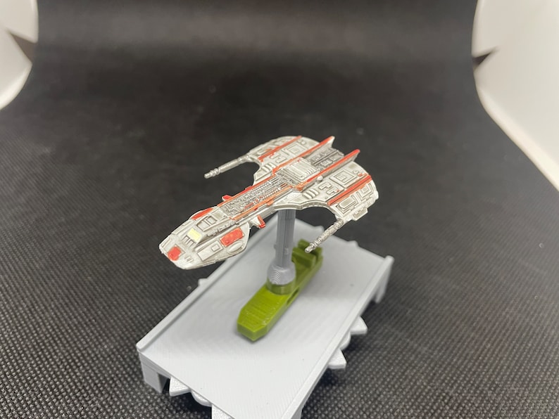 May include: A white and red spaceship model with a gray base. The spaceship has a detailed design with a variety of textures and shapes.