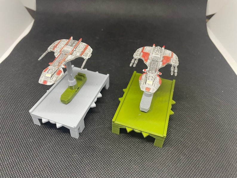 May include: Two miniature spaceships painted in white, red, and gray, with one on a gray base and the other on a green base.