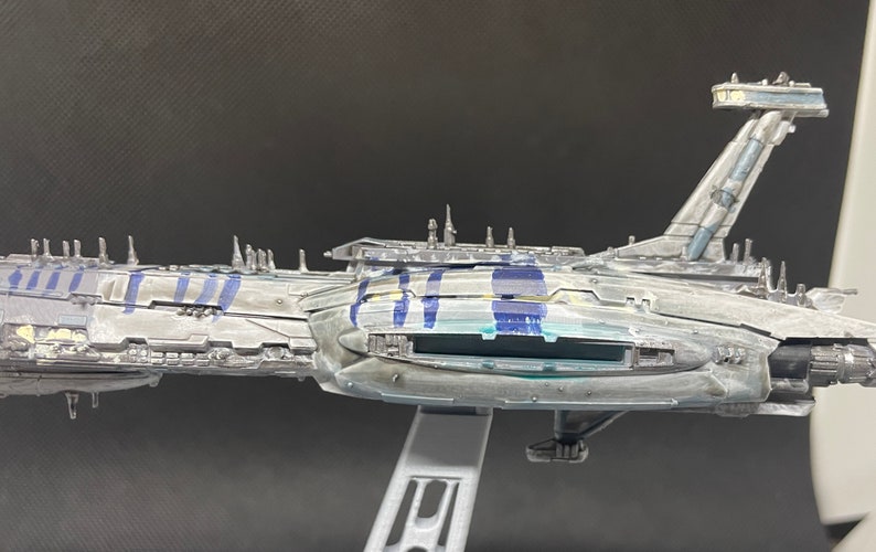 Puede incluir: Un modelo detallado de una gran nave espacial gris con marcas azules y amarillas. La nave espacial tiene un cuerpo largo y estrecho con un gran motor rectangular en la parte trasera. El modelo est&aacute; hecho de pl&aacute;stico y est&aacute; pintado en un estilo realista.