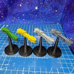 Può includere: Quattro modelli in miniatura di navicelle spaziali in verde, giallo, grigio chiaro e grigio scuro, ciascuno montato su un supporto nero. I modelli sono esposti su uno sfondo blu con un motivo a stelle e una griglia blu.