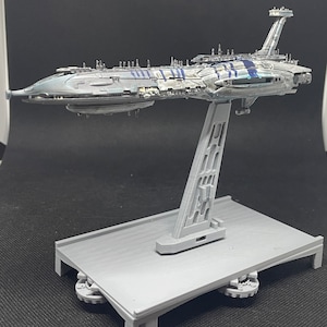 Puede incluir: Un modelo gris y azul de una nave espacial en un soporte gris. La nave espacial tiene un cuerpo largo y delgado con una nariz puntiaguda y un ala grande y plana en la parte superior. El soporte es de pl&aacute;stico y tiene una base rectangular.