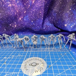 May include: A collection of small, gray, humanoid figurines in various poses, arranged on a blue grid. The figurines appear to be holding weapons or tools. The background is a blue fabric with a starry pattern. The logo "PRINTEDSTARSHIPS.COM" is visible.
