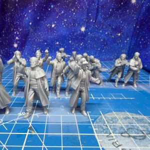 May include: A collection of gray miniature figures, possibly for a tabletop game or diorama. The figures are in various poses, some with arms raised, others in motion. The background is a blue surface with a starry pattern.