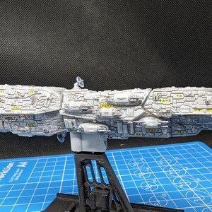 May include: A white model spaceship with yellow details, mounted on a black stand. The spaceship is detailed with a variety of textures and shapes.