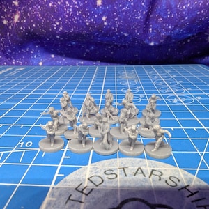May include: A collection of small, gray plastic miniature figures, possibly for tabletop gaming. The figures are in various action poses and are mounted on circular bases. The background is a blue cutting mat with grid lines and a starry fabric.