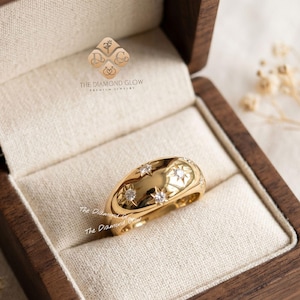 May include: A gold ring with a domed design, featuring star and round-cut diamond embellishments. The ring is presented in a wooden jewellery box with a cream-coloured lining. The Diamond Glow logo is visible.