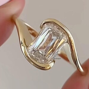 May include: A gold engagement ring featuring a large, clear emerald-cut diamond set in a twisted band.