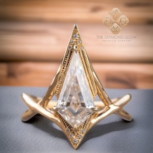 Peut inclure: Une bague de fiançailles en or avec un grand diamant triangulaire clair serti dans une monture géométrique pointue. La bague est rehaussée de petits diamants autour de la pierre centrale.