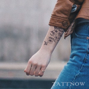 Könnte beinhalten: Ein temporäres Tattoo mit einem floralen Design auf dem Arm einer Person. Das Tattoo ist schwarzweiß und zeigt eine Ansammlung von Blumen mit Stielen und Blättern.