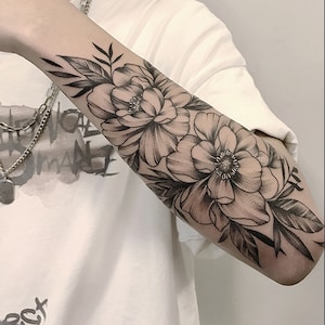May include: A black and white tattoo of two large flowers with leaves on a person's forearm.