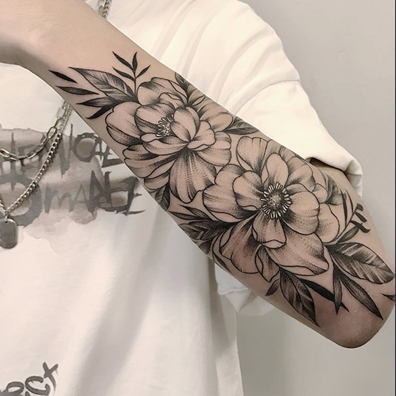 May include: A black and white tattoo of two large flowers with leaves on a person's forearm.
