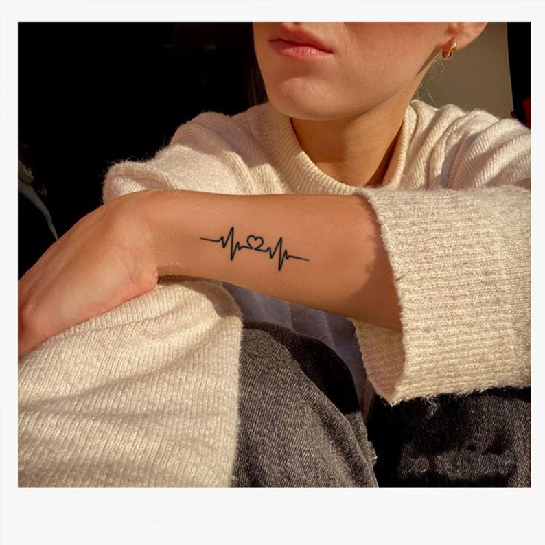 May include: A black line heart beat tattoo on a person's wrist.