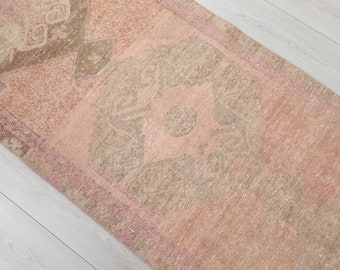 May include: A rectangular, distressed-look rug with a central medallion design. The rug features a color palette of soft pinks, beige, and brown, with a faded, vintage appearance. The rug's pattern includes geometric and floral elements.