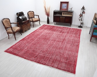 May include: A large rectangular area rug featuring a deep red color palette with a distressed, faded texture throughout. The rug displays a subtle, intricate pattern woven into the fabric, with visible fringe detailing along the shorter edges.