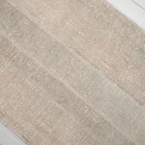 May include: A close-up of a beige and white woven rug with a textured surface. The rug has a subtle sheen and a striped pattern.