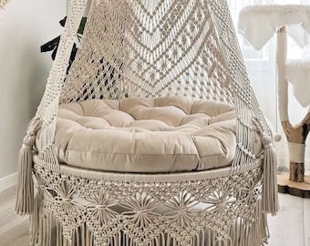 May include: A white macrame hanging chair with a round cushion. The chair has a fringe border and a geometric pattern.