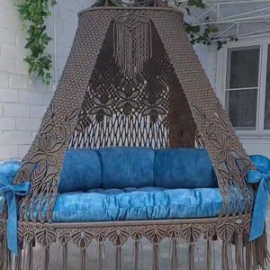 May include: A brown macrame hammock swing with a blue cushion and fringe trim. The hammock is hanging from the ceiling and has a canopy.