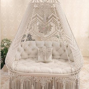 May include: A white macrame hammock swing with a white cushion and pillow. The hammock is decorated with tassels and has a canopy.