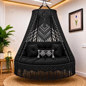 Peut inclure: Un fauteuil suspendu en macramé noir avec un siège et un dossier ronds et rembourrés. La chaise présente une frange décorative le long du bord inférieur et est suspendue à une chaîne. Comprend des coussins noirs et un oreiller décoratif à motifs blancs.