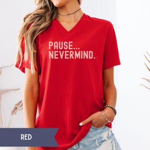 K&ouml;nnte beinhalten: Rotes V-Ausschnitt-T-Shirt mit dem wei&szlig;en Text "PAUSE... NEVERMIND.". Das Shirt hat kurze &Auml;rmel und ist einfarbig rot. Das Wort "RED" befindet sich in einem dunkelblauen Banner am unteren Bildrand.