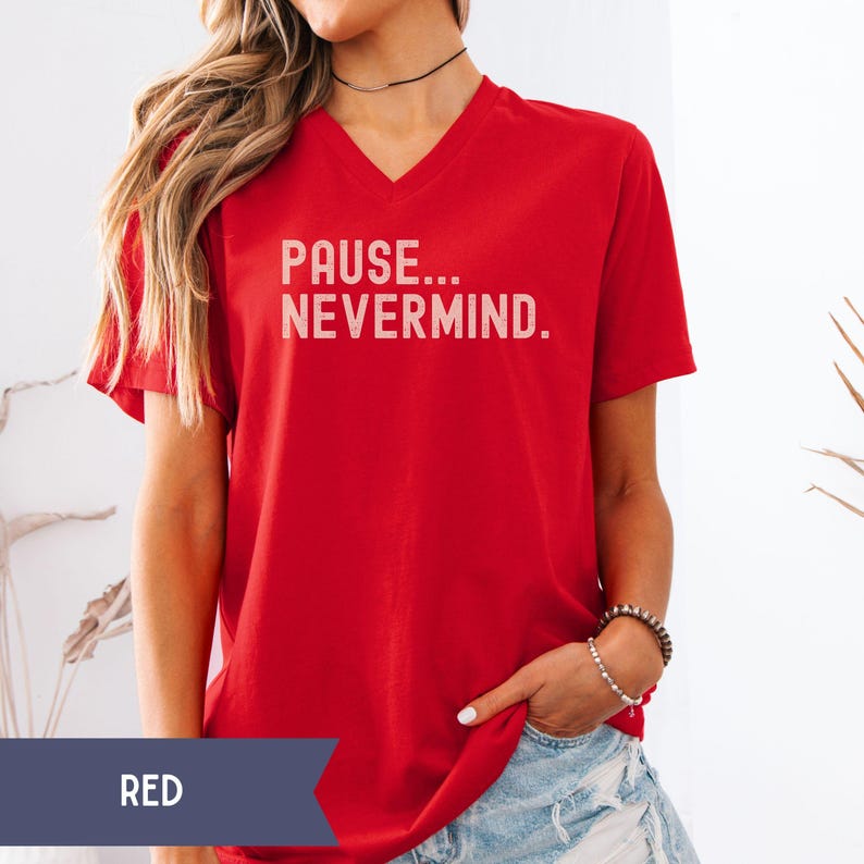 K&ouml;nnte beinhalten: Rotes V-Ausschnitt-T-Shirt mit dem wei&szlig;en Text "PAUSE... NEVERMIND.". Das Shirt hat kurze &Auml;rmel und ist einfarbig rot. Das Wort "RED" befindet sich in einem dunkelblauen Banner am unteren Bildrand.