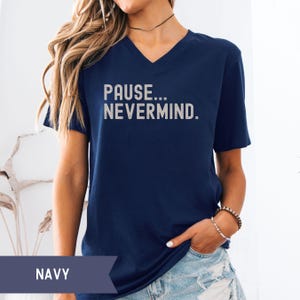 K&ouml;nnte beinhalten: Marineblaues V-Ausschnitt-T-Shirt mit dem Text "PAUSE... NEVERMIND." in hellgrauer Farbe aufgedruckt. Das Shirt hat eine marineblaue Volltonfarbe. Das Shirt ist ein l&auml;ssiger Stil.