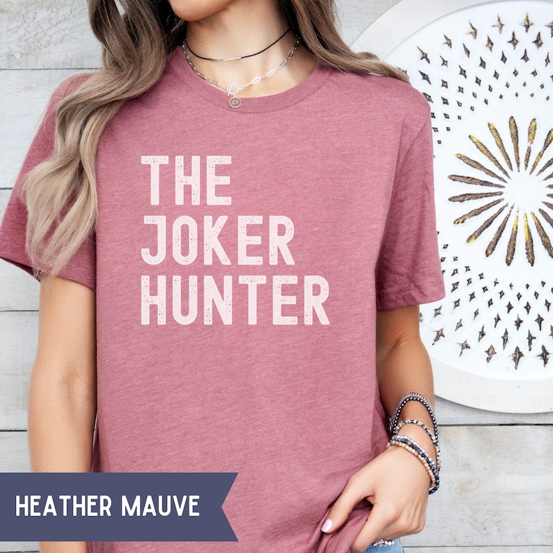 Pode incluir: T-shirt cor malva mesclado com o texto branco "THE JOKER HUNTER". A camisa tem mangas curtas e gola redonda. As palavras "HEATHER MAUVE" s&atilde;o exibidas em uma faixa na parte inferior da imagem.