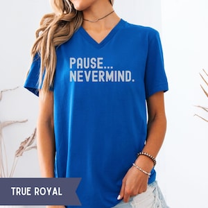 K&ouml;nnte beinhalten: Ein k&ouml;nigsblaues V-Ausschnitt-T-Shirt mit dem wei&szlig;en Text "PAUSE... NEVERMIND.". Das Shirt ist einfarbig und hat kurze &Auml;rmel. Das Model tr&auml;gt Armb&auml;nder und eine Halskette.