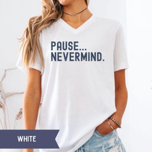 K&ouml;nnte beinhalten: Wei&szlig;es V-Ausschnitt-T-Shirt mit dem Text "PAUSE... NEVERMIND." in Marineblau. Das Shirt ist ein l&auml;ssiger Stil, geeignet f&uuml;r den Alltag. Das Wort "WHITE" wird auf einem dunkelblauen Banner am unteren Bildrand angezeigt.