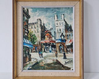 Könnte beinhalten: Ein Ölgemälde in einem Holzrahmen zeigt eine Straßenszene mit Gebäuden, einer Windmühle und Figuren. Das Kunstwerk verwendet Blau-, Braun- und Weißtöne, mit einer Signatur unten rechts. Der Rahmen hat eine hellbeige Leinenstruktur.