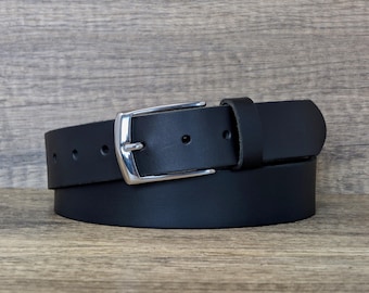 Puede incluir: Un cinturón de cuero negro con una hebilla de metal plateado pulido de una sola púa. La correa del cinturón tiene un acabado mate liso e incluye una serie de orificios de ajuste circulares espaciados uniformemente a lo largo.