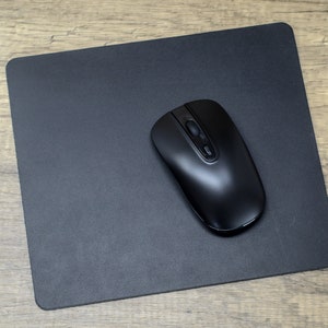 May include: A black computer mouse on a black mouse pad. The mouse has a smooth, rounded design and two buttons.